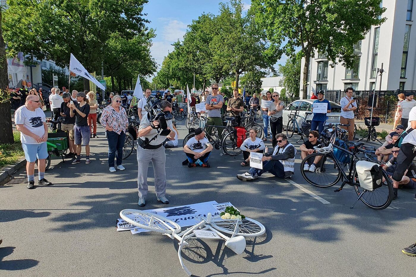 Menschen sitzen bei einer Mahnwache auf dem Boden um ein weißes Fahrrad