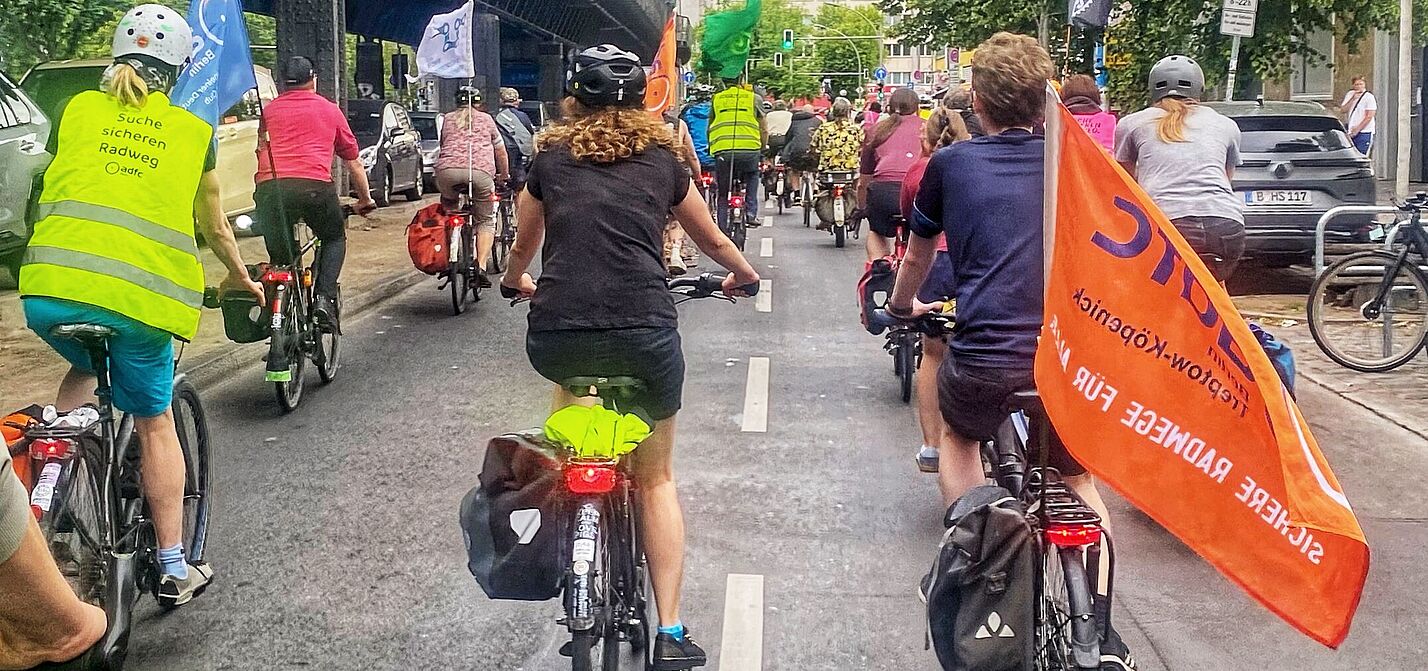 Respect Cyclists am 04. Juni Richtung Friedrichshain-Kreuzberg Eine Gruppe Radfahrende fährt mit Fahnen auf einer Fahrbahn Richtung Kreuzberg. Links im Bild ist die oberirdische U-Bahnlinie 1 zu sehen.