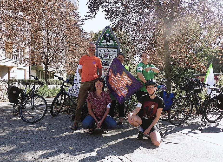 Ordner:innen der Kidical Mass Schöneberg 21.09.2024 am Startort Barbarossaplatz Am Barbarossa stehen auf dem Gehweg Kidical Mass Demo Ordner:innen mit Armbinden und Fahnen