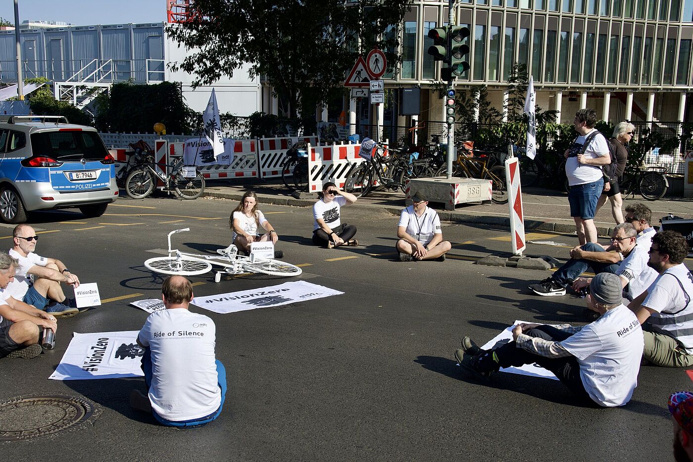 Menschen sitzen um ein weißes Fahrrad auf der Straße bei einer Gedenkminute