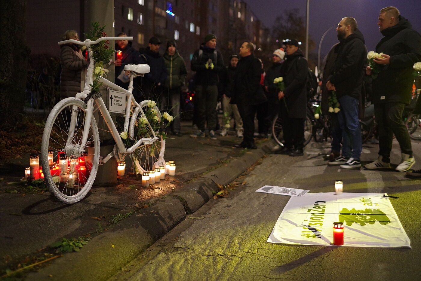 ein weißes Geisterrad mit Grabkerzen und einer Vision Zero Fahne am Straßenrand