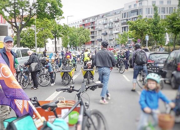 Auf dem Vorarlberger Damm in Berlin Schöneberg stehen vor der Jugendverkehrsschule am Sachsendamm Teilnehmende der Kidical Mass bei einer Zwischenkundgebung.