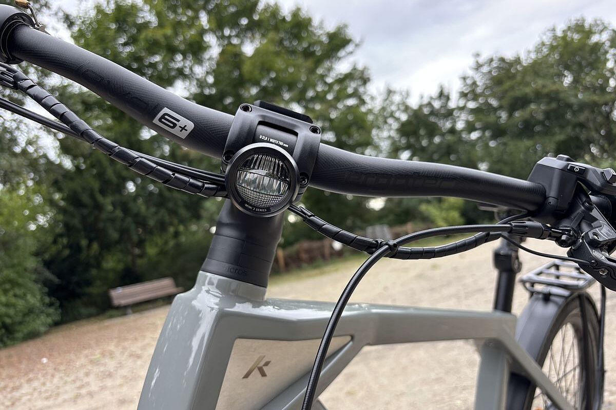Großaufnahme eines am Lenker montierten, runden Scheinwerfers mit schwarzem Gehäuse an einem grauen Rad. 